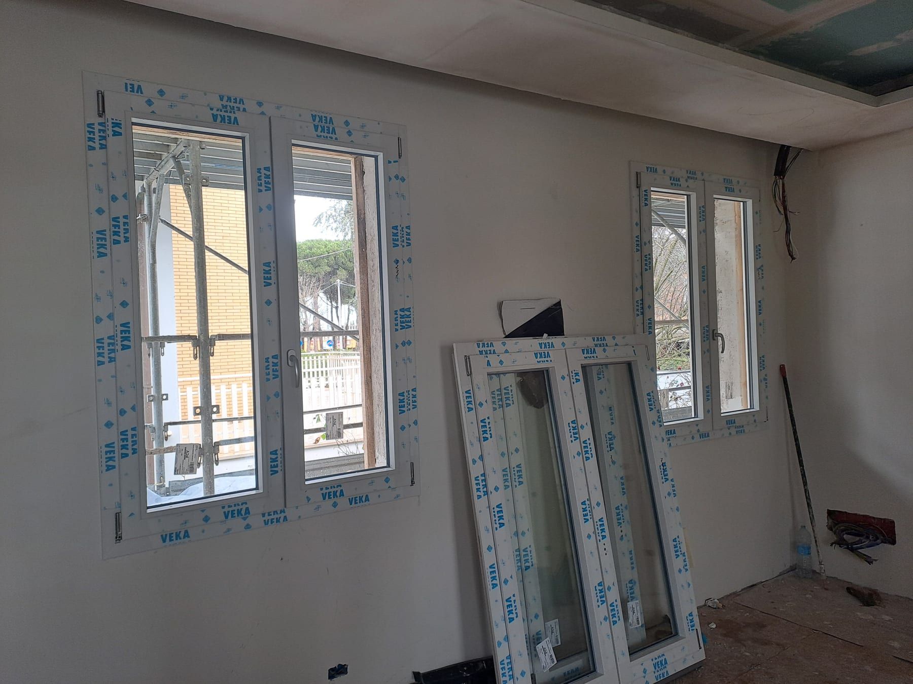 Due finestre bianche appena montate in un cantiere, con le pellicole protettive ancora sui profili