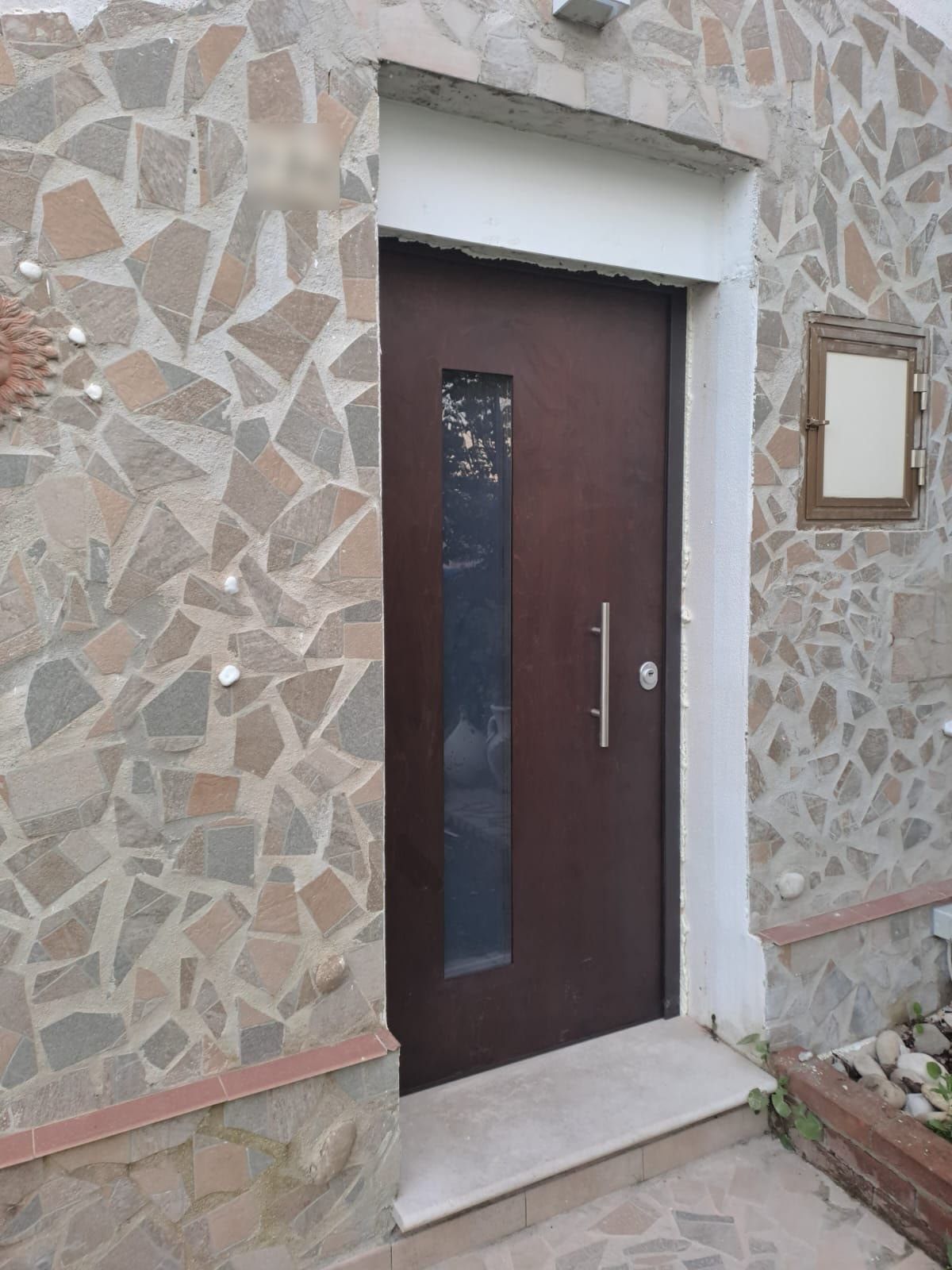 Portoncino d’ingresso marrone scuro con vetro verticale e maniglione, su una casa rivestita in pietra
