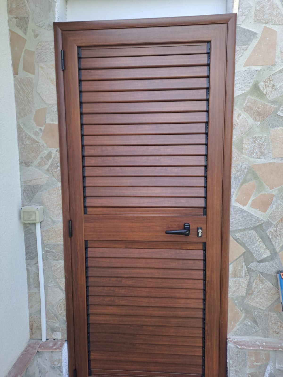 Persiana a un’anta color legno, con maniglia e serratura, su un ingresso rivestito in pietra